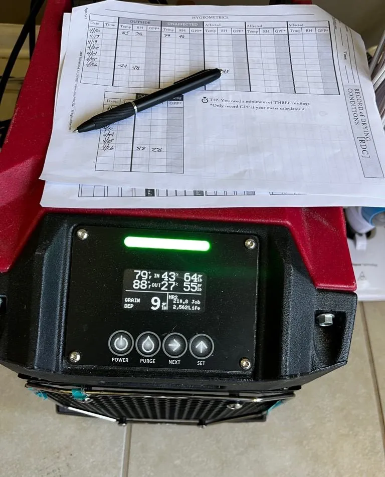 Handwritten daily drying log sheet resting on top of a dehumidifier display