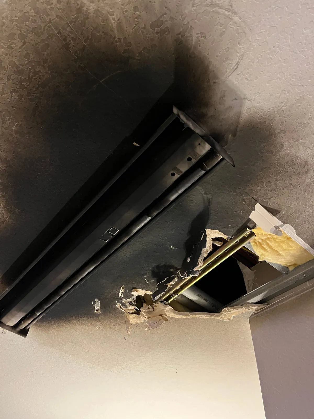 Burned ceiling light fixture with soot spreading across the ceiling and a hole into the attic