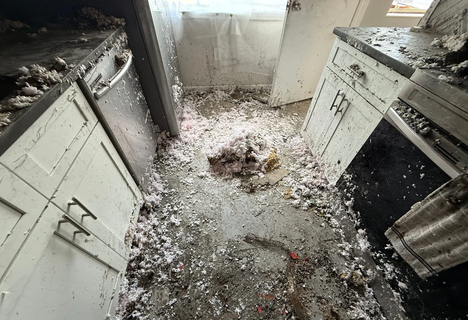 Burned kitchen with fallen insulation and debris across the floor between soot-stained cabinets