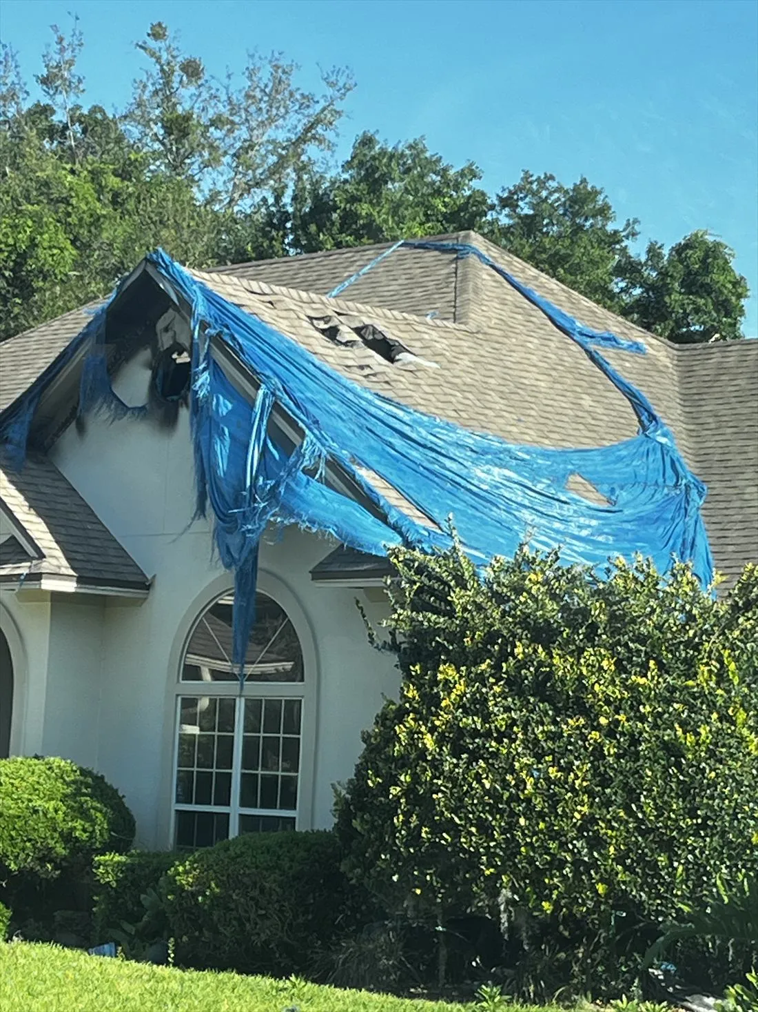 Torn blue tarp over a damaged roof with a scorched gable on a two-story house